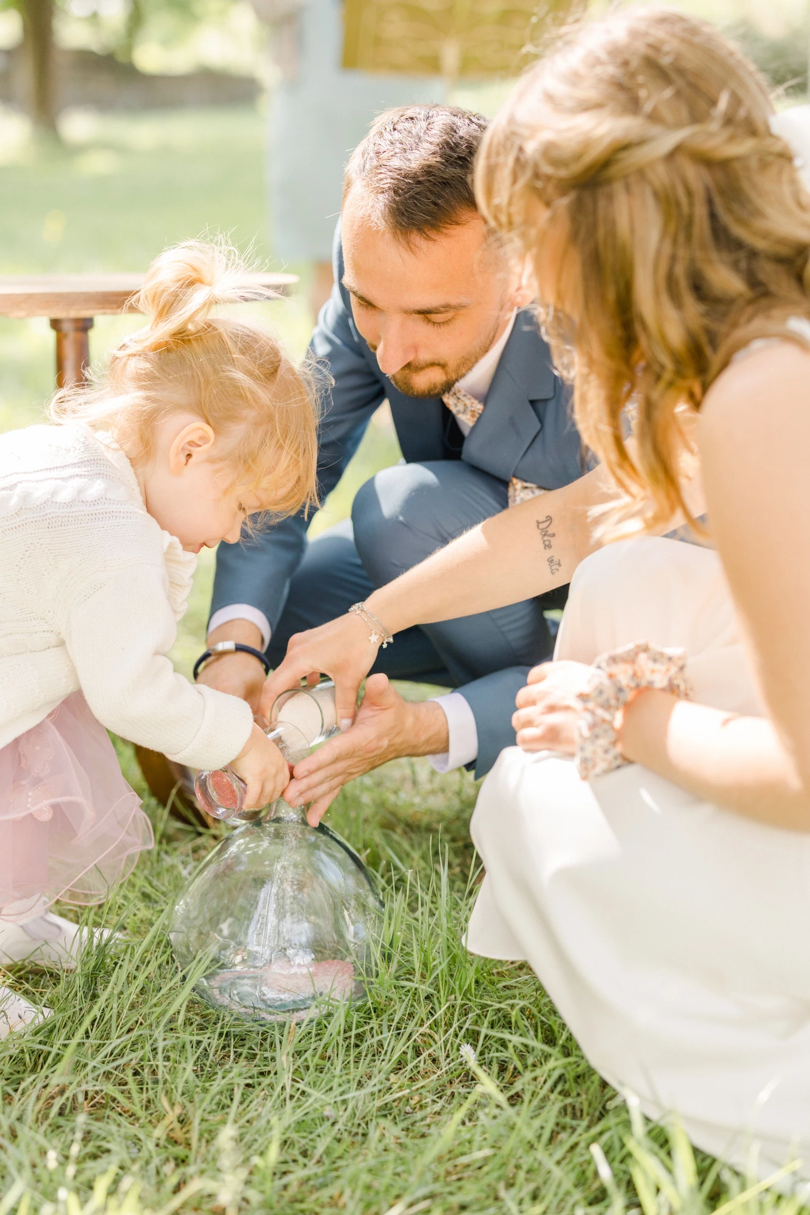 Jeunes mariés et leur enfant versant du sable lors d'une cérémonie laïque en extérieur