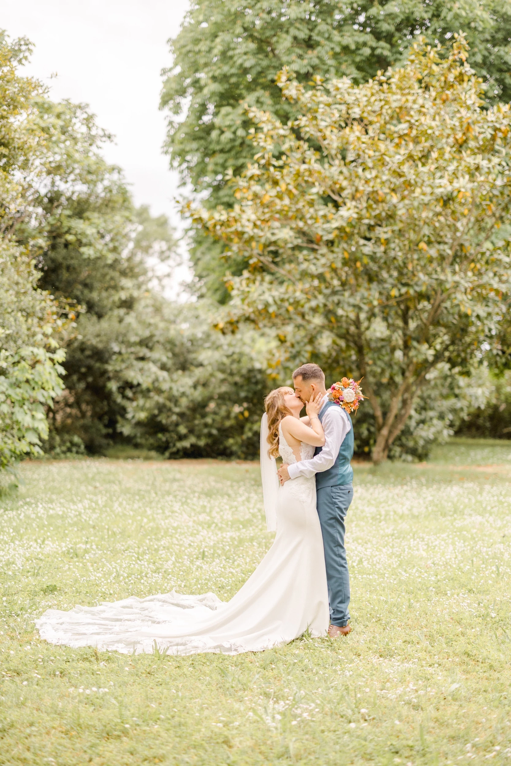 Couple de mariés s'embrassant dans un parc verdoyant, robe blanche à longue traîne