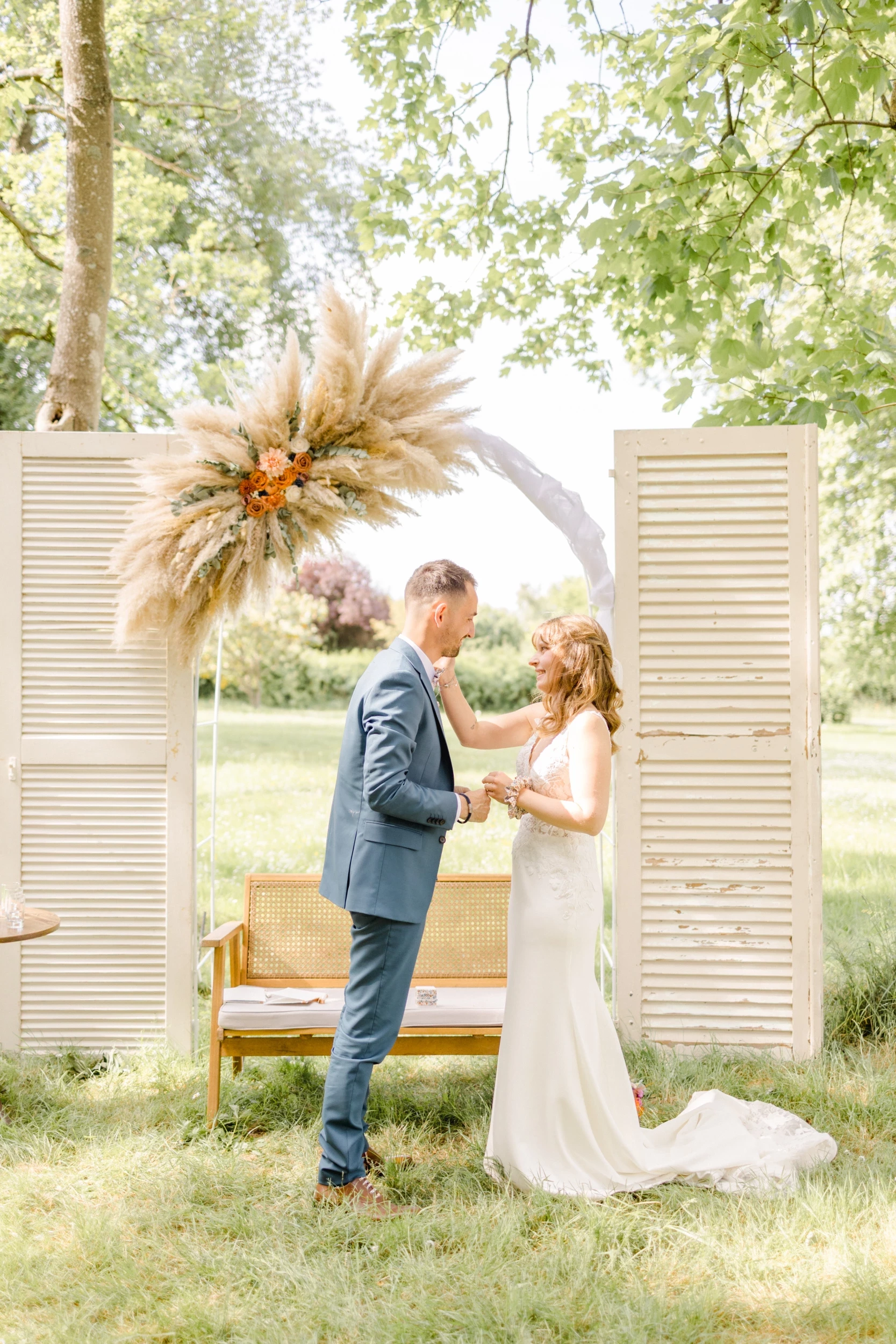 Couple de mariés se tenant la main sous une arche de pampas lors d'une cérémonie laïque champêtre