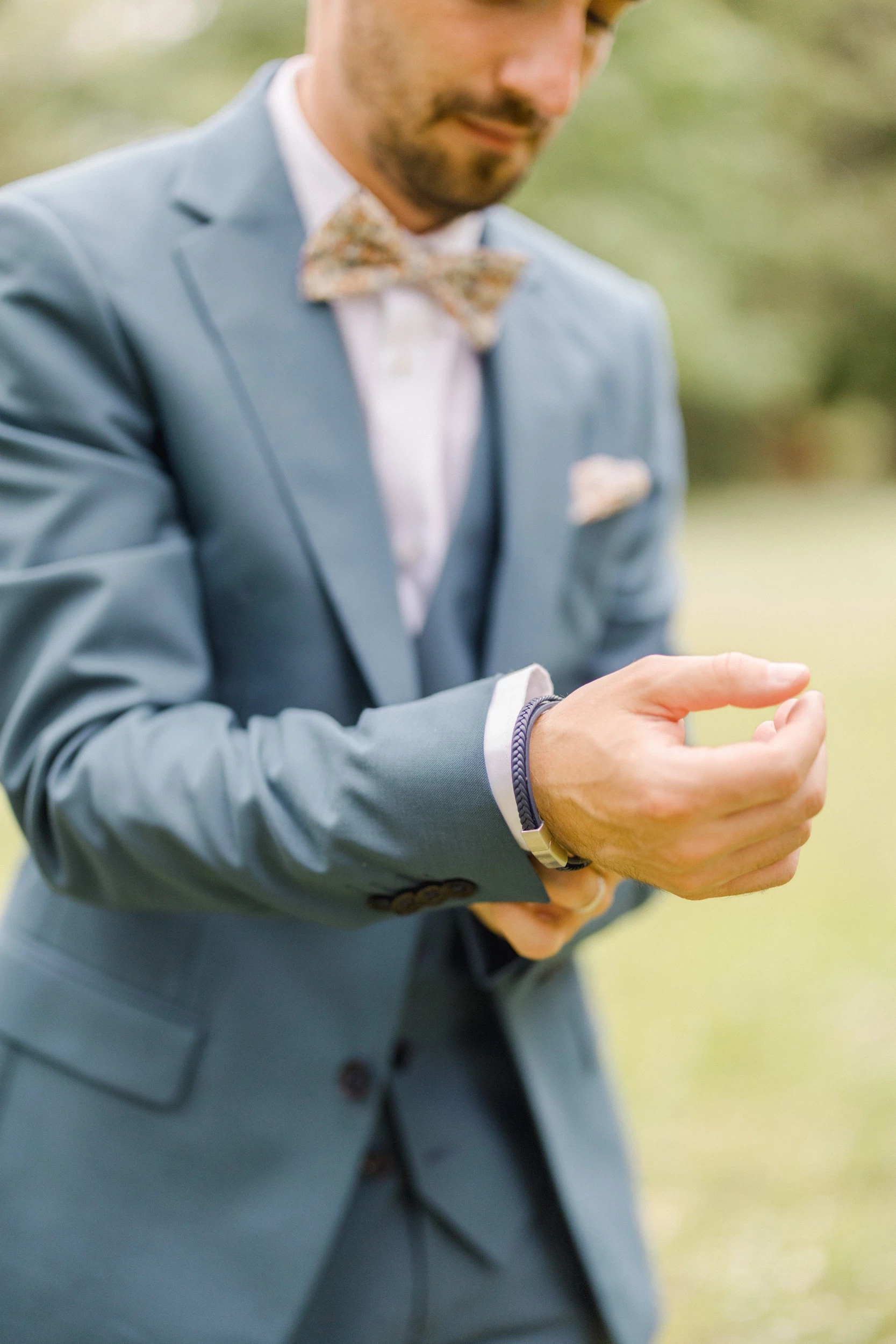 Marié en costume gris et nœud papillon beige ajustant ses boutons de manchette lors des préparatifs