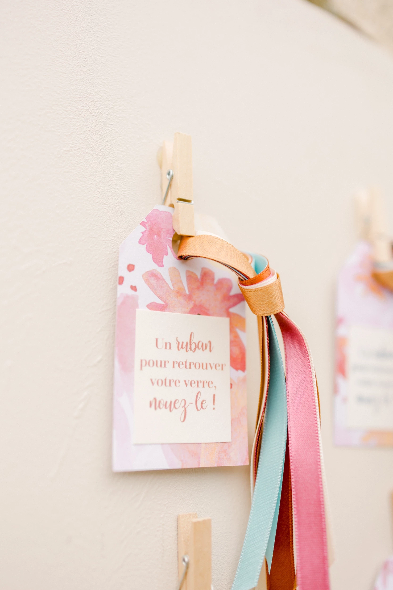 Étiquette de mariage rose ornée de fleurs aquarelle et rubans colorés accrochée sur un mur blanc
