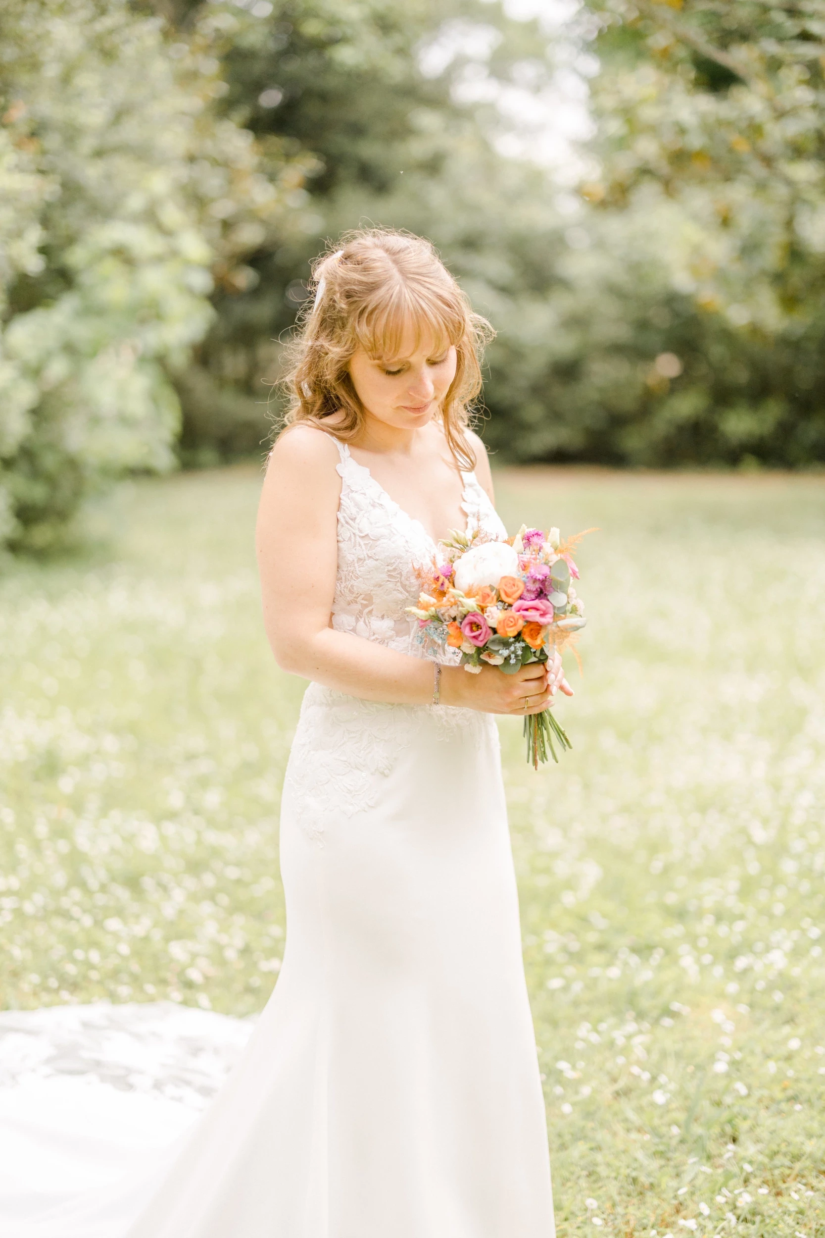Mariée en robe blanche tenant délicatement son bouquet champêtre dans un jardin verdoyant