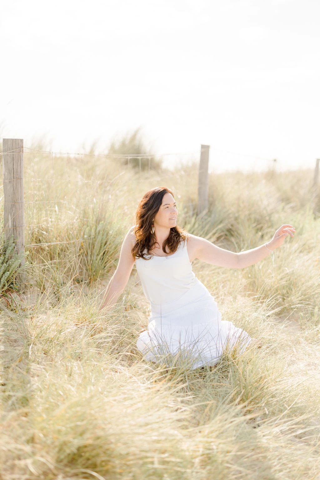 Femme en robe blanche assise dans les dunes, baignée de lumière douce et dorée