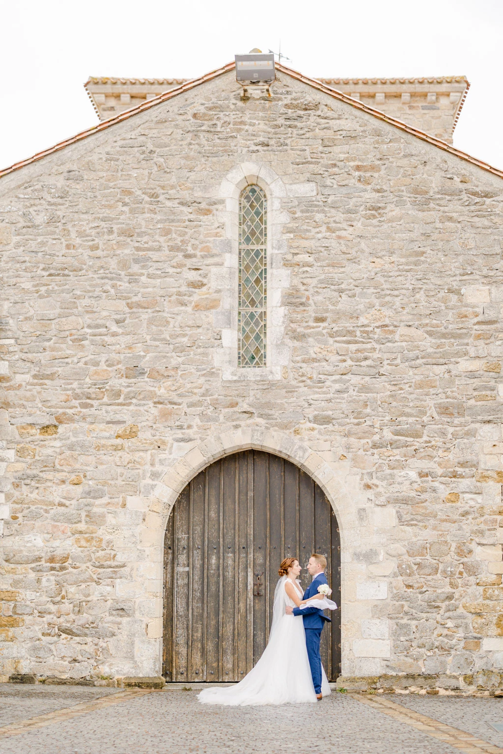 Couple de mariés échangeant leurs vœux sous l'arche d'une église en pierre ancienne lors de leur cérémonie