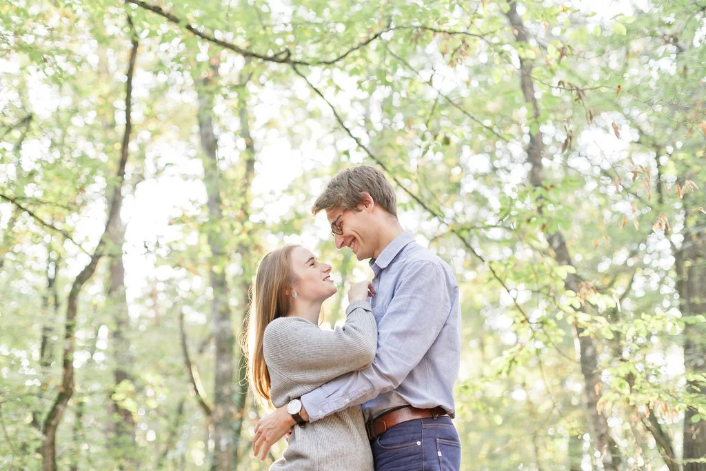 Séance couple en forêt : jeune femme et homme s'enlacent tendrement sous la lumière dorée des feuillages, ambiance intime et romantique