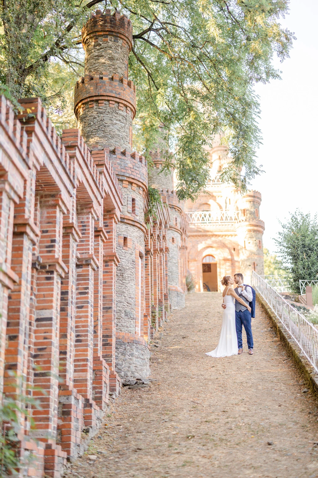 Couple de mariés marchant main dans la main le long d'une allée de château aux murs de briques