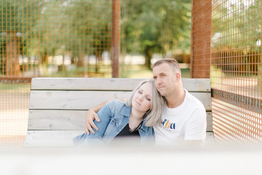 Séance couple portrait en extérieur : jeune femme et homme assis sur banc blanc, tendresse et complicité dans parc verdoyant, lumière naturelle douce et élégante