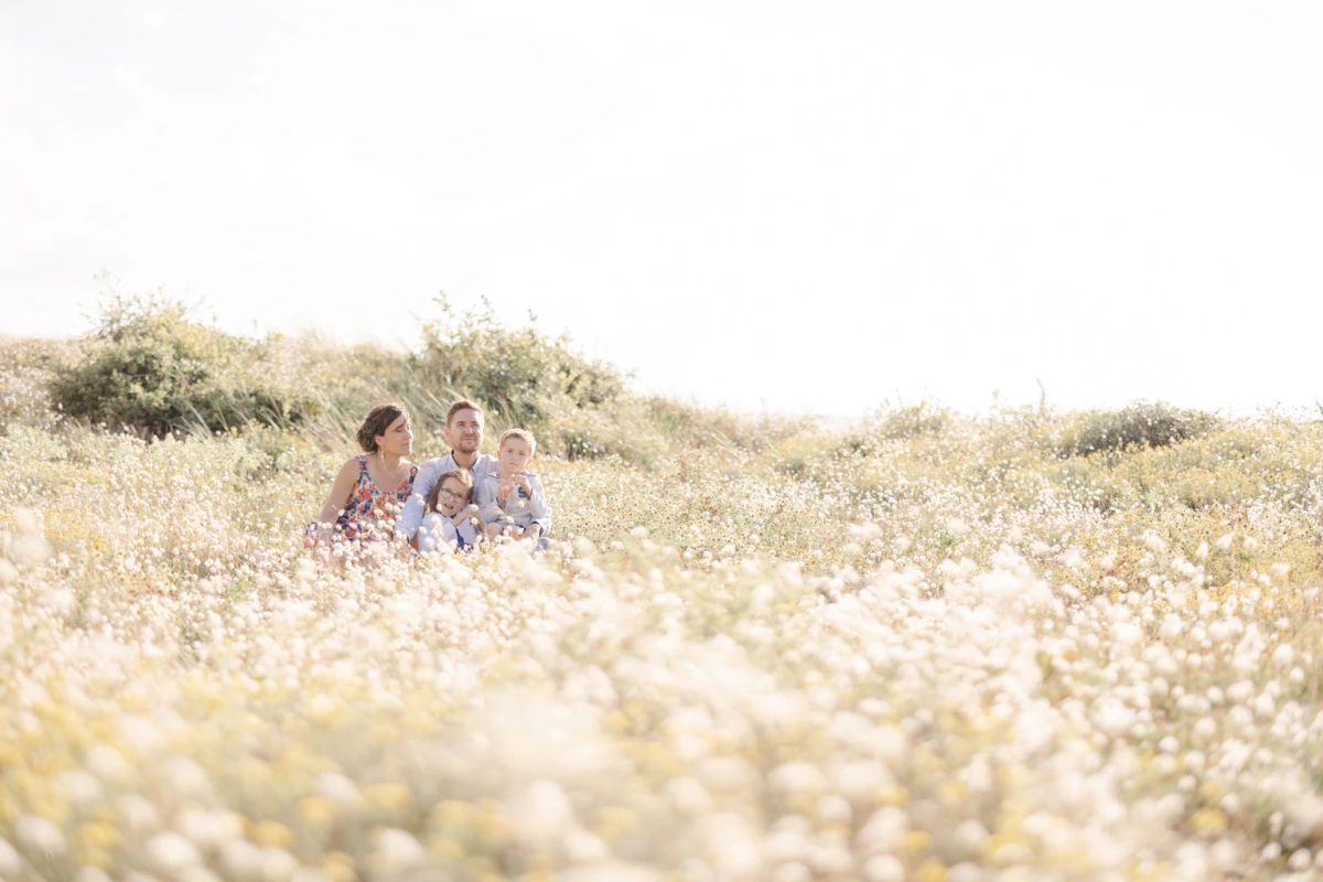 Mère et ses deux enfants assis dans un champ de marguerites baigné de lumière dorée estivale