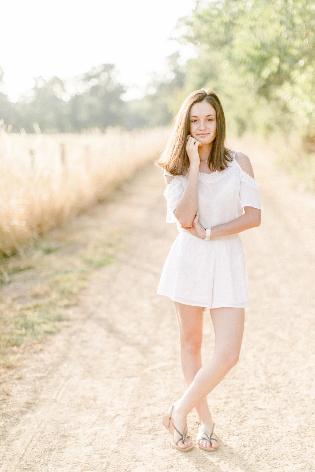 Jeune fille souriante en robe blanche sur un chemin de campagne ensoleillé
