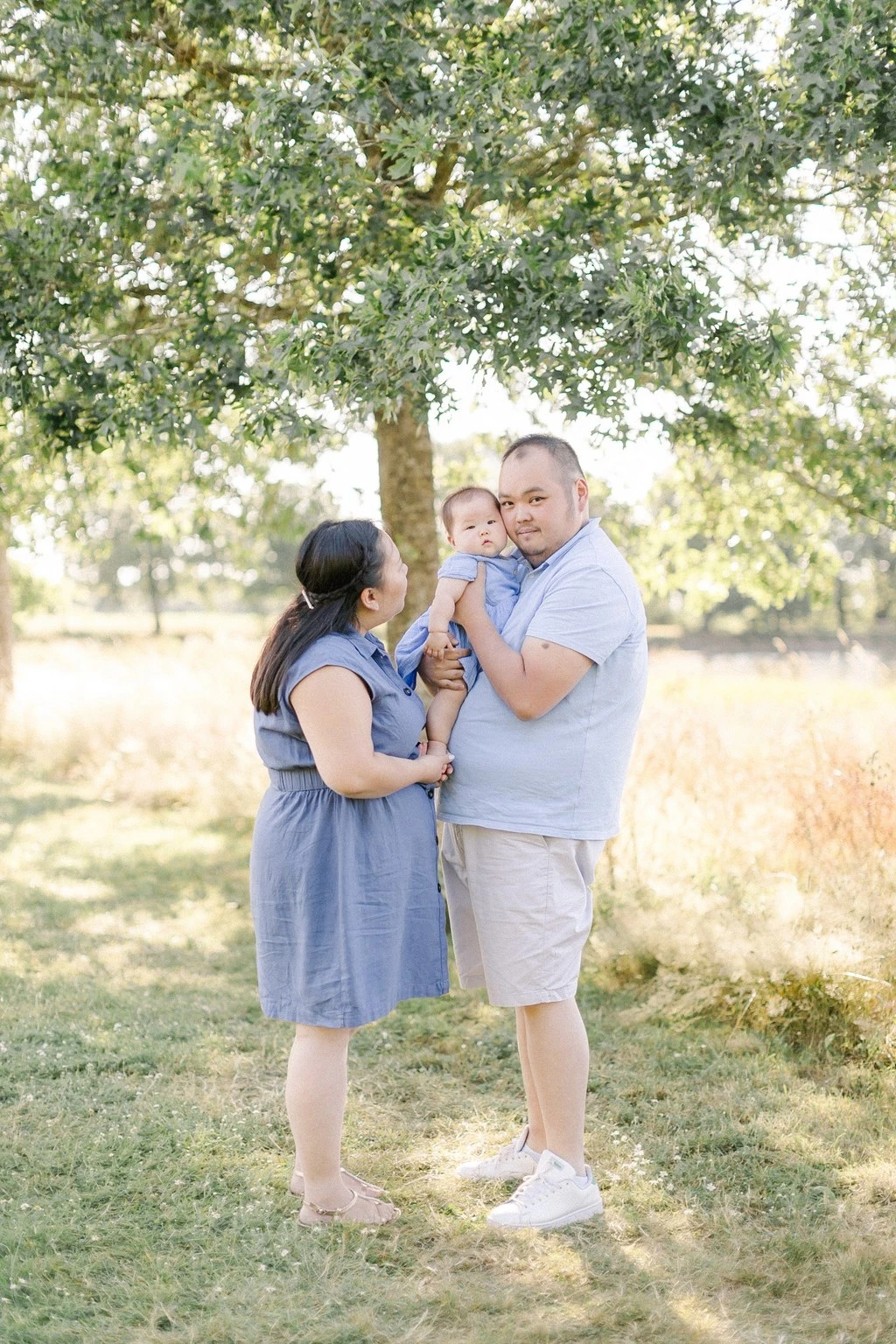 Séance photo famille en extérieur : parents et enfant souriants sous un arbre majestueux, lumière dorée et naturelle, ambiance de tendresse et complicité