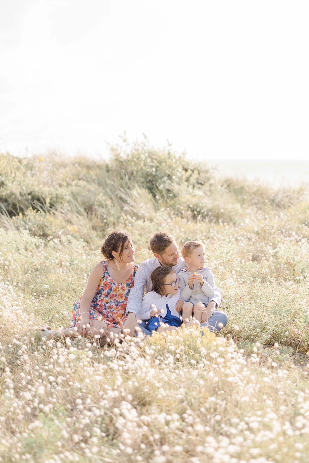 Famille avec trois enfants assis ensemble dans un champ de fleurs sauvages blanches en pleine nature