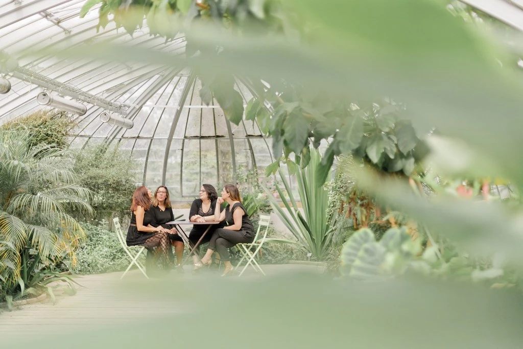 Séance famille en serre : trois femmes assises dans une véranda végétalisée, ambiance intime et lumineuse