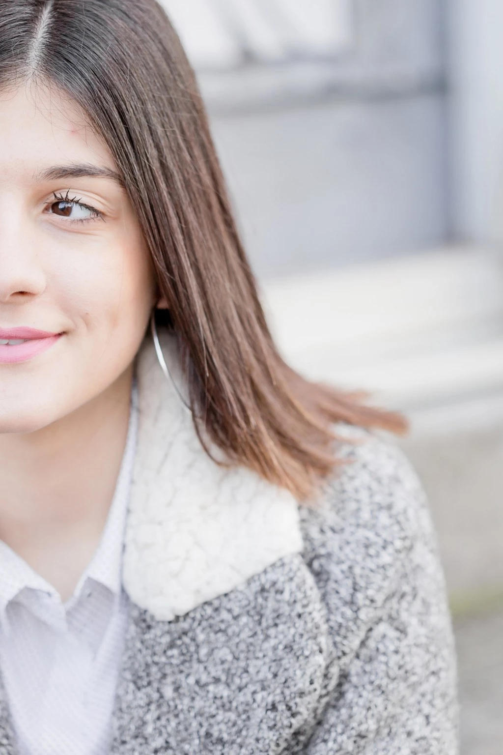 Portrait d'une adolescente souriante aux cheveux bruns longs, vêtue d'un pull gris et d'une chemise blanche