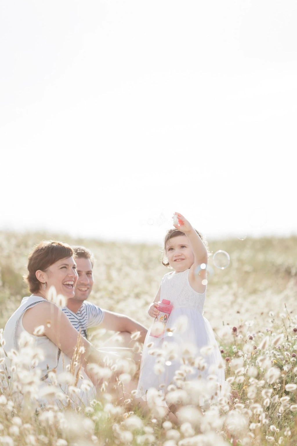 Séance photo famille en extérieur dans un champ de coton blanc, trois personnes souriantes baignées de lumière dorée, ambiance tendre et lumineuse en Vendée