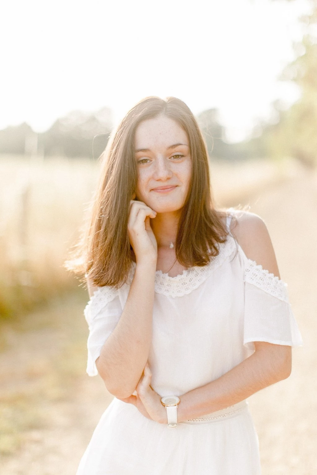 Portrait de jeune femme en robe blanche avec détails en dentelle, posant avec tendresse dans un champ doré baigné de lumière dorée, ambiance sereine et intemporelle