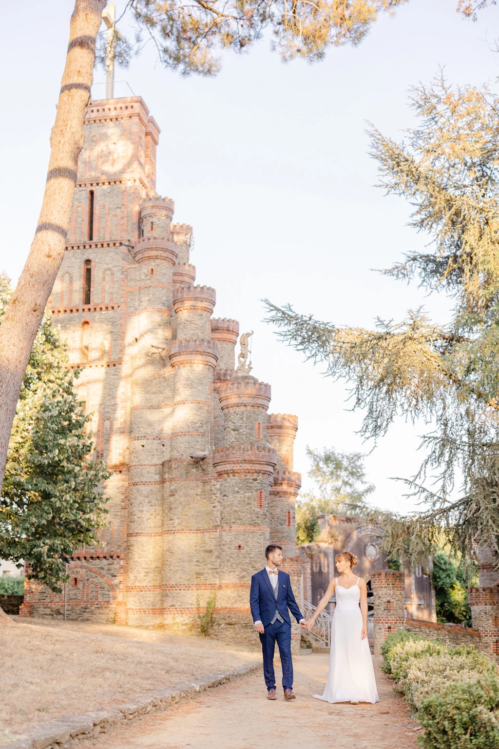 Séance photo mariage devant tour en briques rouges, couple élégant en tenue de cérémonie, lumière dorée automne, ambiance romantique et intemporelle
