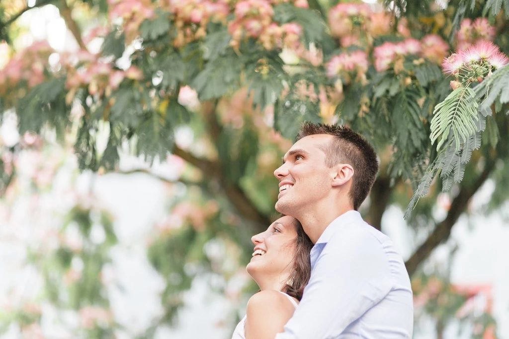 Séance photo de couple sous un arbre fleuri, moment de tendresse et complicité, lumière douce naturelle, ambiance printemps élégante et intemporelle