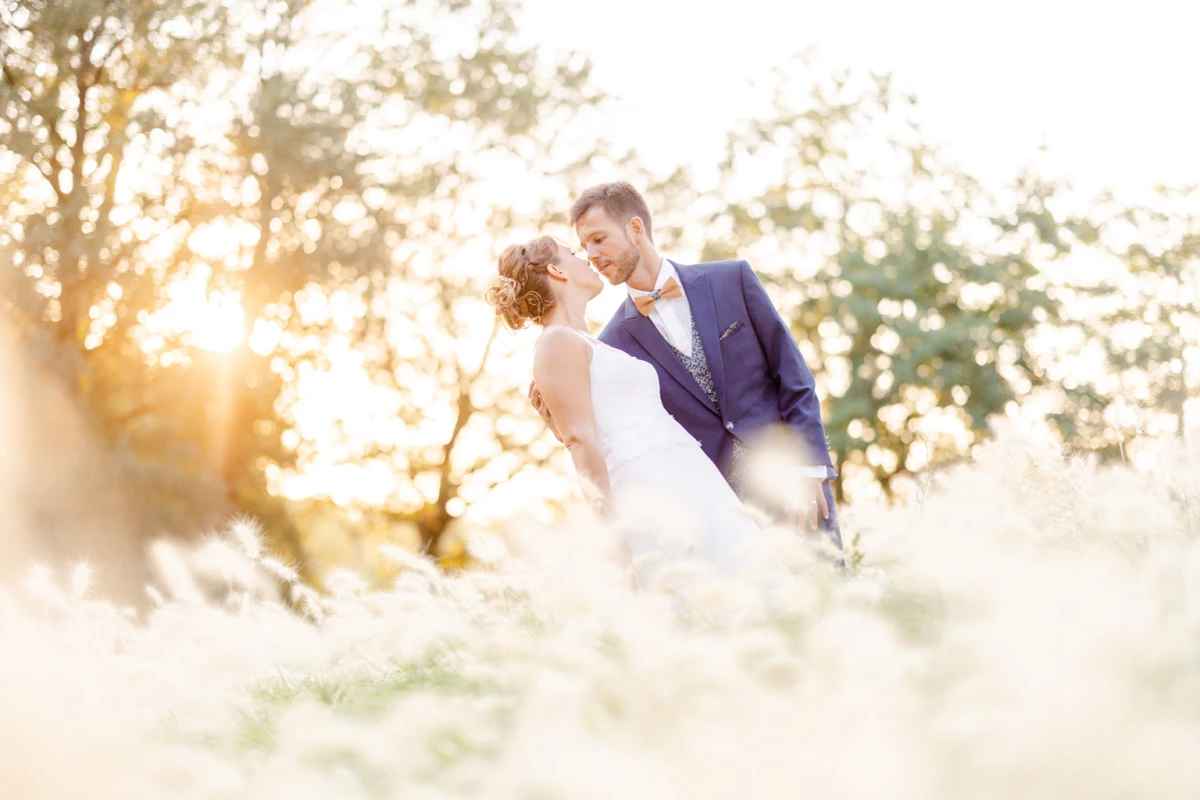 Séance photo mariage en plein air avec mariés s'embrassant tendrement dans une lumière dorée et floue, entourés de végétation, ambiance romantique et intemporelle en Vendée
