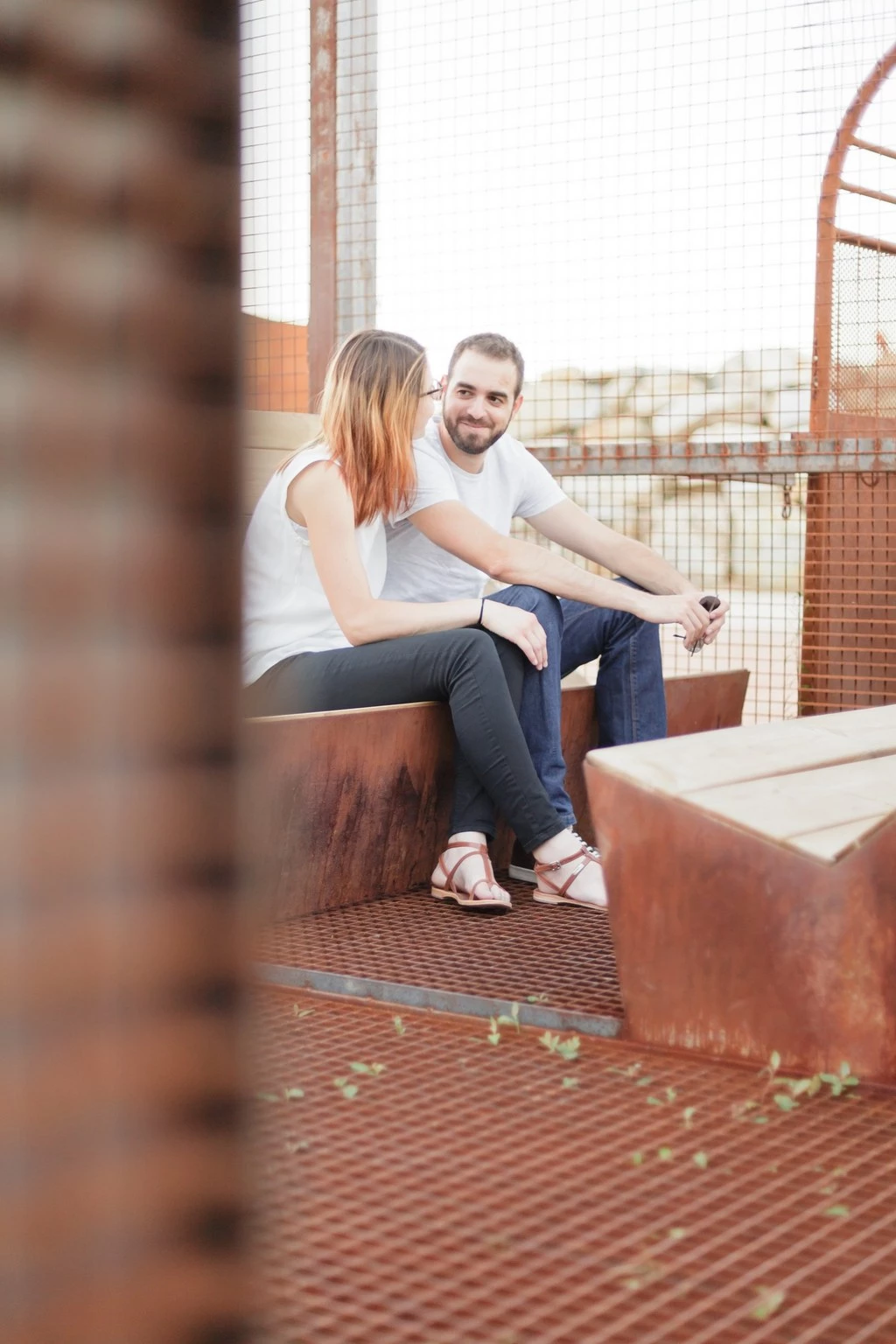Séance portrait couple en toiture : jeune femme et homme assis complices, lumière dorée, ambiance intime et tendre, architecture brique en arrière-plan