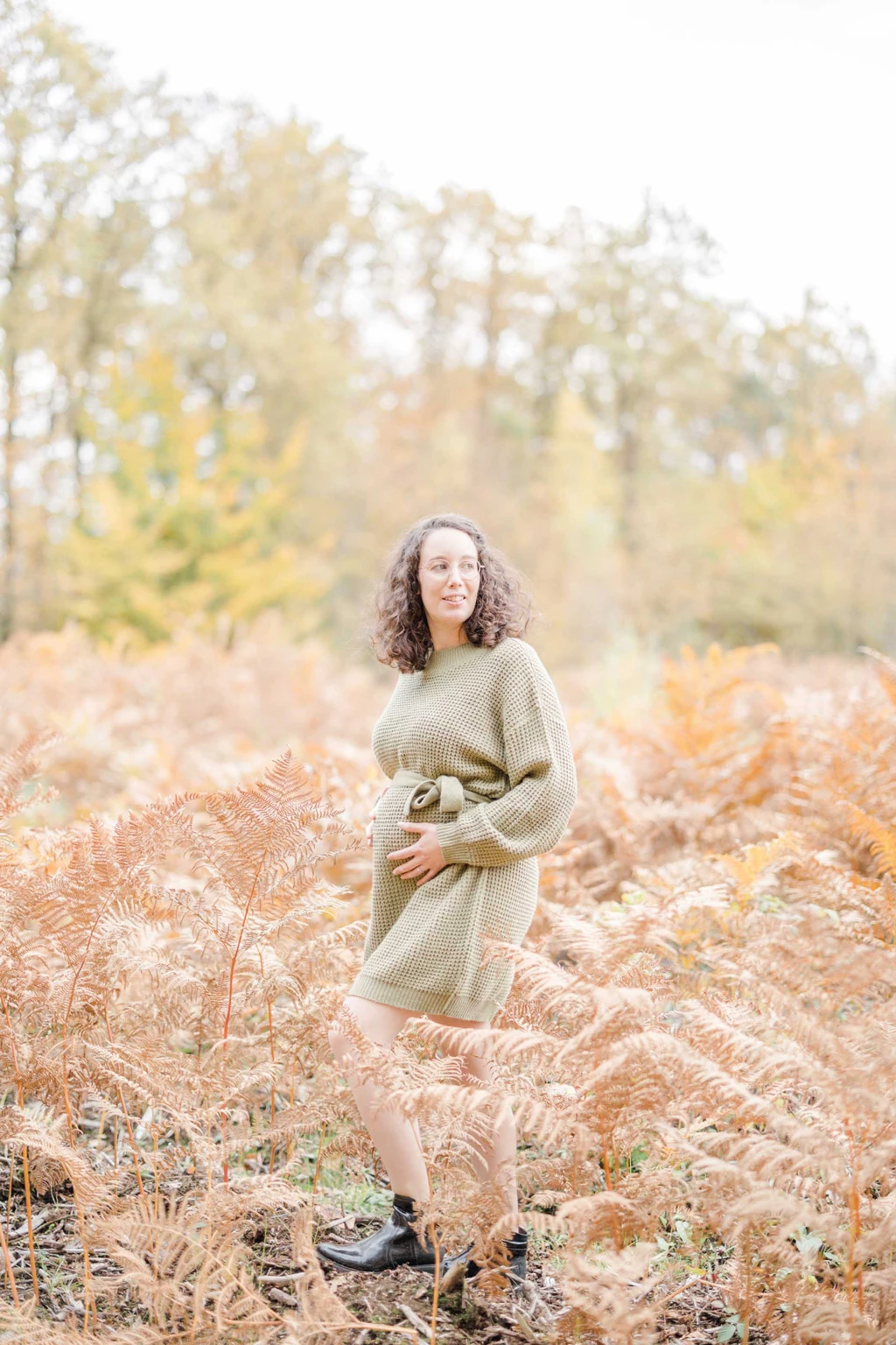 Femme en robe pull beige posant dans un champ de fougères automnales dorées en forêt
