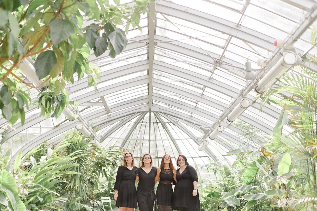 Séance photo famille quatre femmes en robes noires dans une serre victorienne lumineuse, ambiance intemporelle et élégante