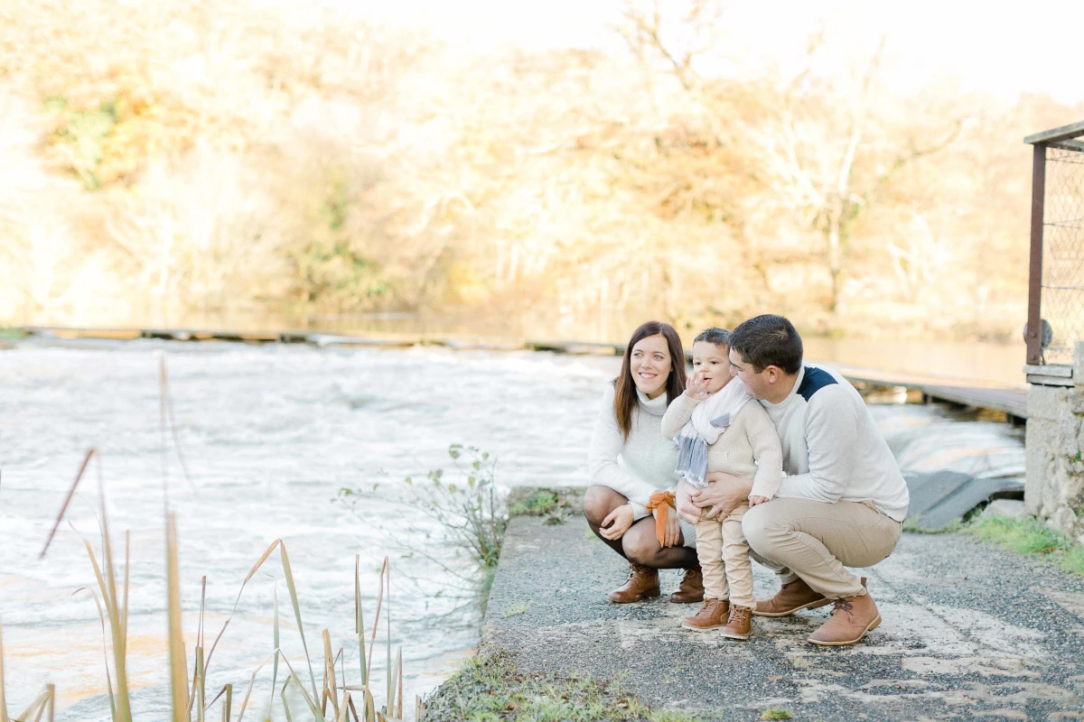 Séance photo famille en bord de l'eau : jeune couple avec enfant en bas âge, complicité tendre sur fond de nature apaisante, lumière dorée et ambiance intime