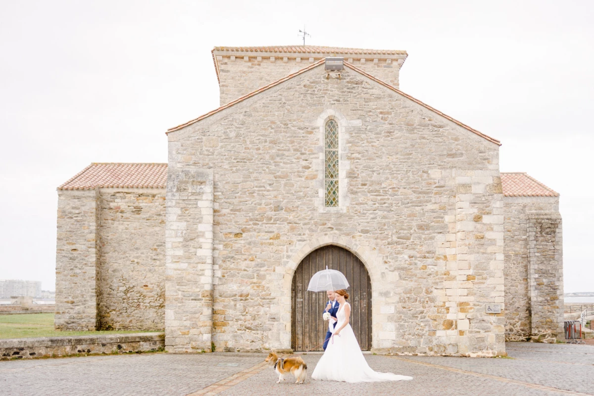Couple de mariés devant une église en pierre ancienne avec un chien, photographie de mariage élégante