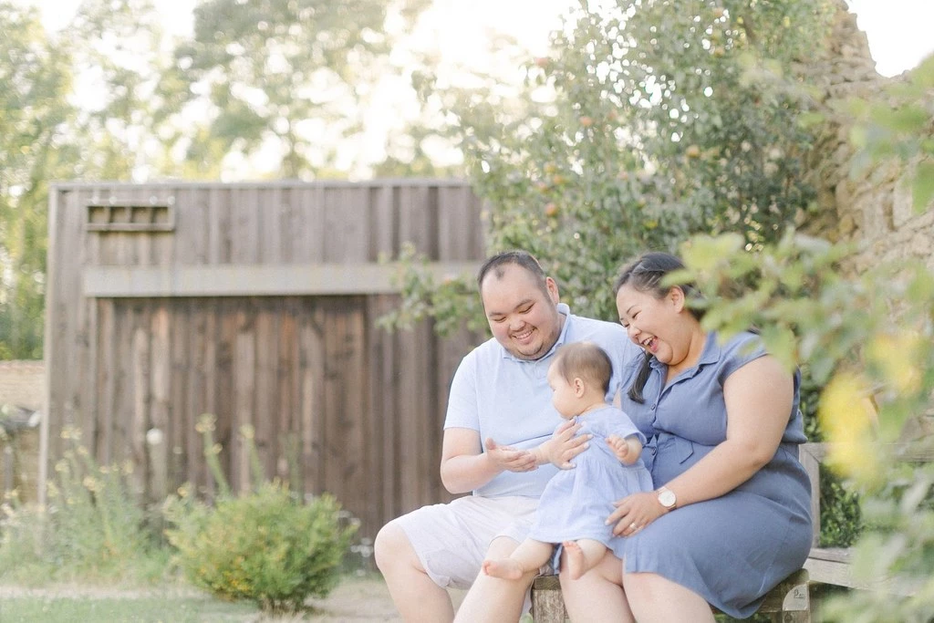 Séance photo famille en extérieur : deux parents et leur jeune enfant assis ensemble dans un jardin verdoyant, captured dans une ambiance de tendresse et de complicité naturelle