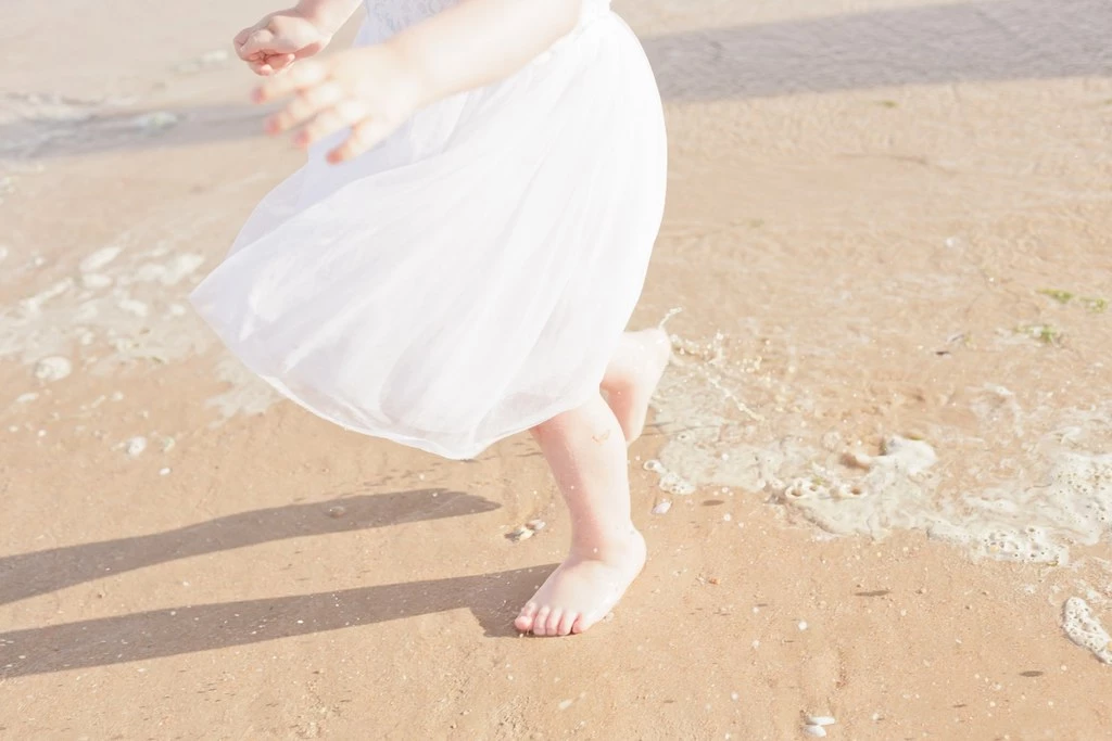 Séance famille à la plage : enfant en robe blanche courant pieds nus dans les vagues au coucher de soleil, moment de tendresse et de liberté enfantine en Vendée