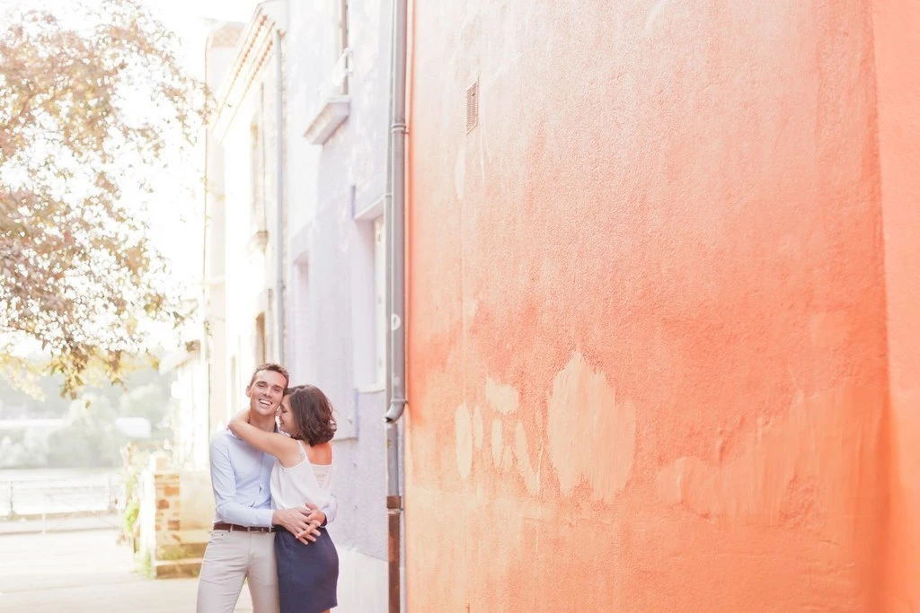 Séance de couple tendresse devant mur rose pêche, lumière naturelle dorée, intimité et complicité dans ambiance intemporelle et élégante