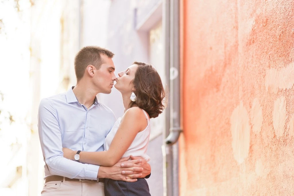 Séance couple tendresse : jeune homme et femme s'embrassant contre mur terracotta, lumière dorée, intimité authentique en extérieur
