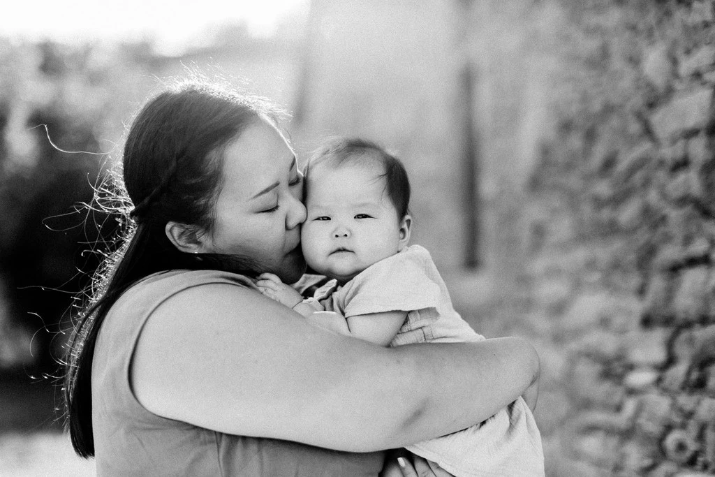 Séance photo famille en noir et blanc : grande sœur tenant tendrement son nouveau-né dans ses bras, moment d'authentique complicité et douceur, luminosité naturelle douce