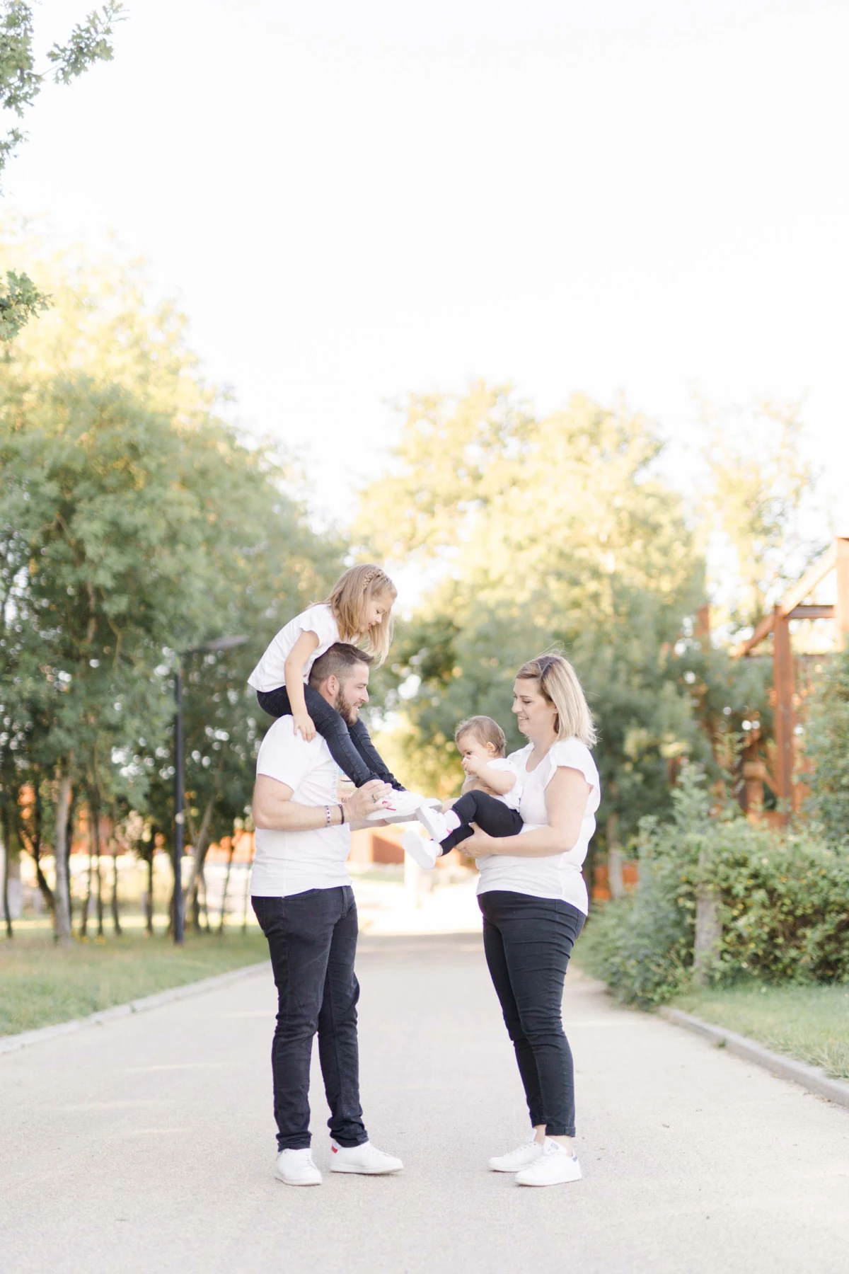 Séance photo famille en extérieur : parents jouant avec leurs deux enfants dans une allée arborée, ambiance joyeuse et complice sous lumière dorée