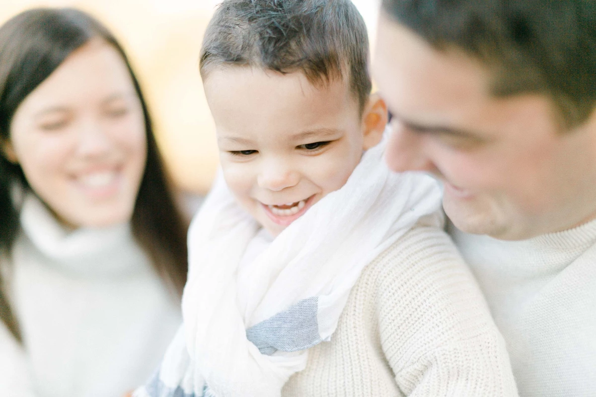 Séance famille en studio : père, mère et petit enfant souriants dans une ambiance lumineuse et chaleureuse, portraiture émotionnelle et intemporelle