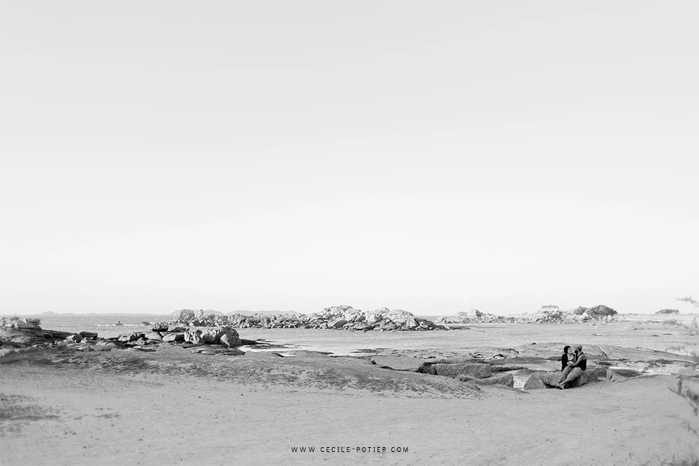 Séance famille en bord de mer, deux silhouettes dans le sable avec vue panoramique, ambiance intemporelle et épurée en noir et blanc