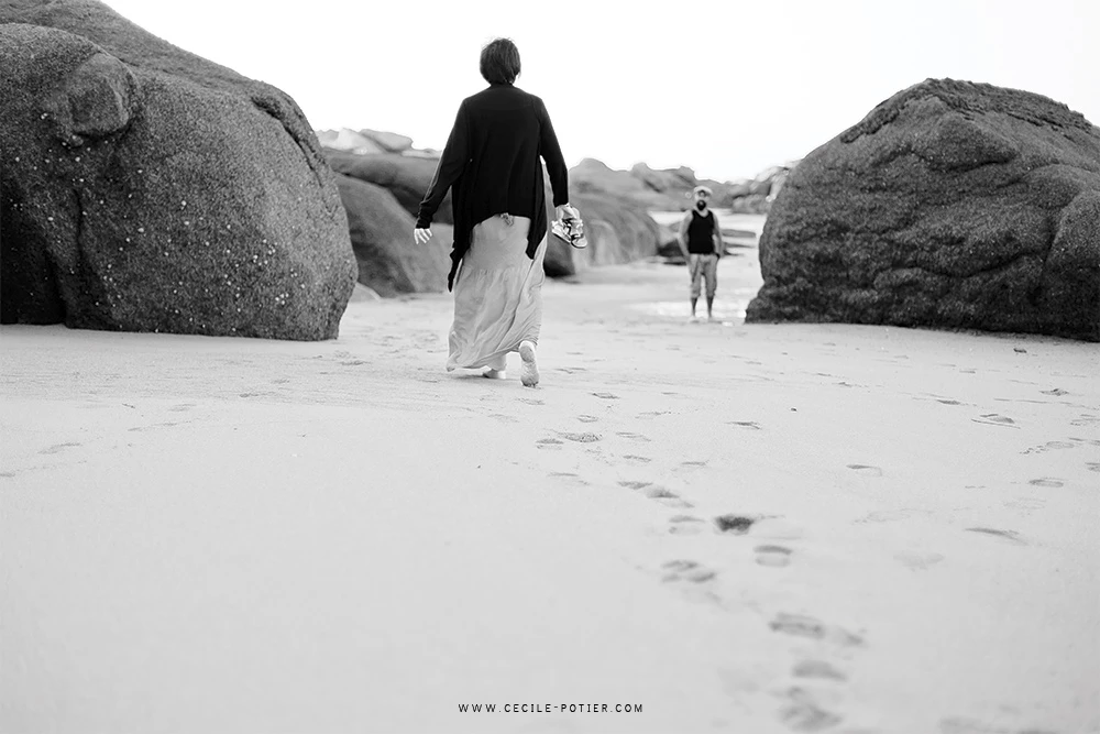 Séance famille à la plage entre rochers granitiques, enfants courant vers l'océan, ambiance intemporelle et émotionnelle en noir et blanc