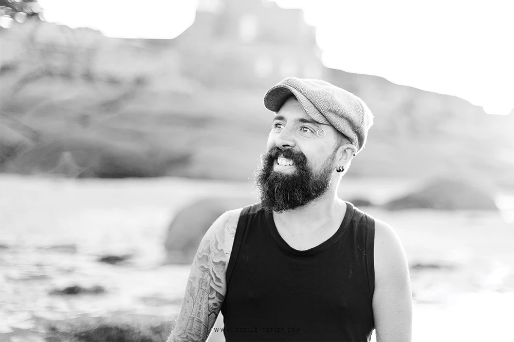 Portrait corporate homme barbu en casual chic face à la mer, lumière naturelle douce, ambiance contemplative et authentique en bord de plage