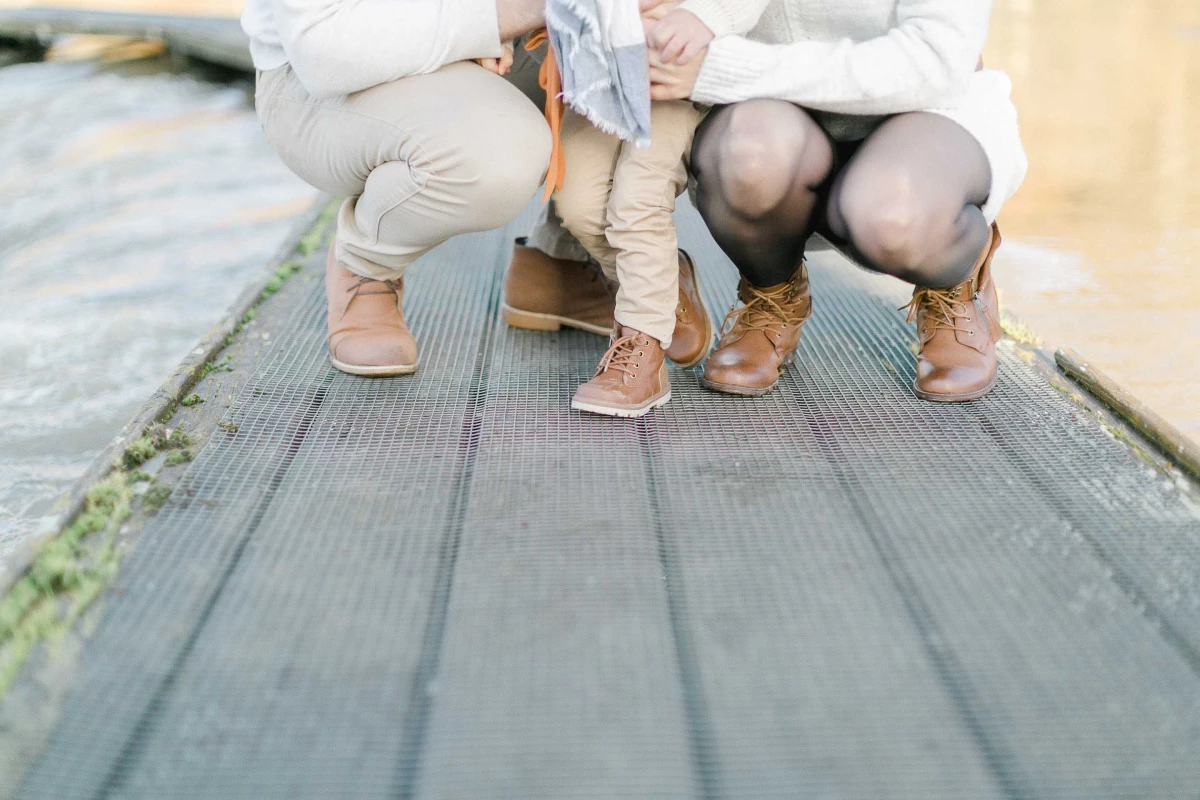 Séance photo famille en extérieur : deux enfants assis côte à côte sur une passerelle en bois, pieds nus, dans une ambiance de complicité tendre et authentique