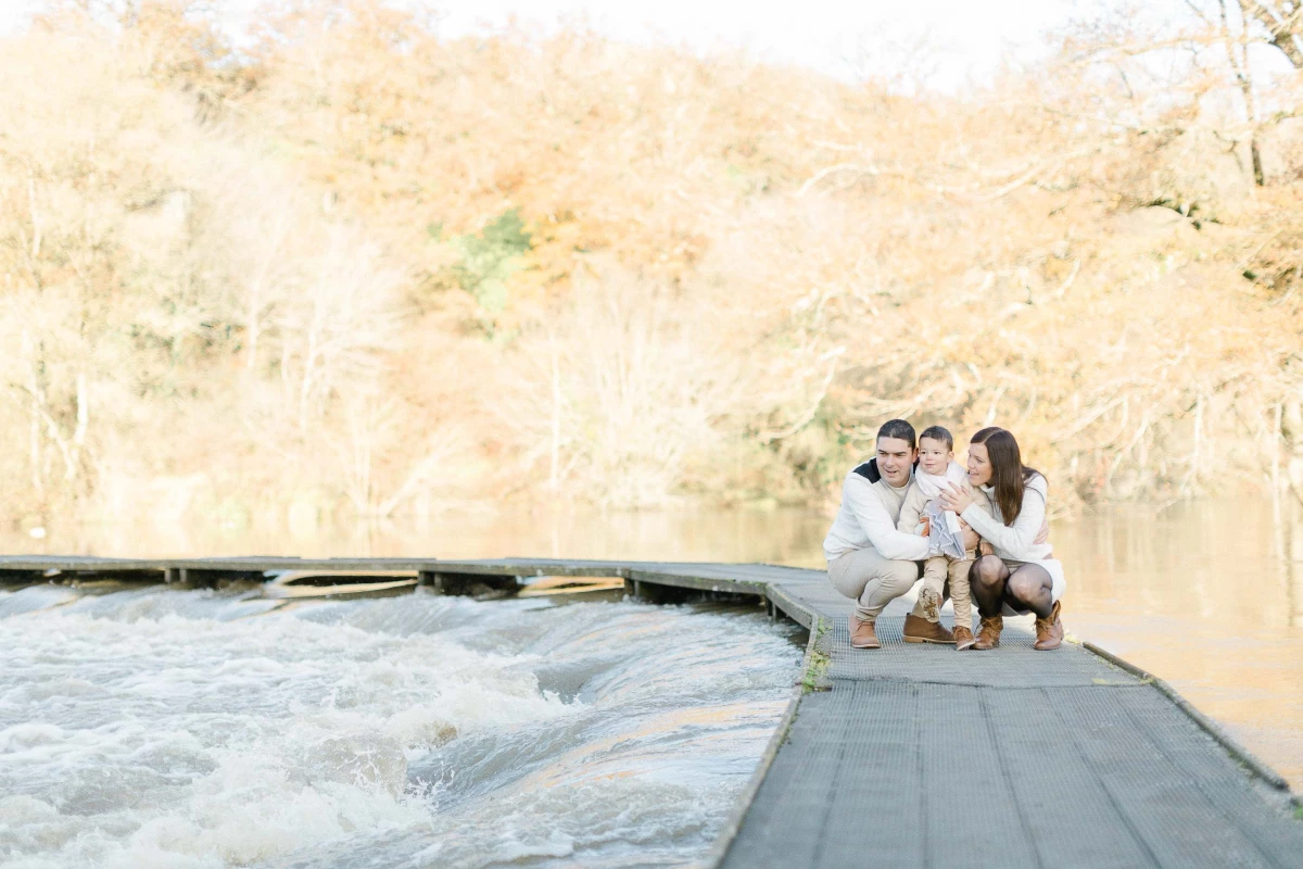 Séance photo famille : trois personnes assises sur une terrasse en bois face à une piscine, baignées de lumière dorée, exprimant complicité et tendresse dans une ambiance intemporelle et élégante