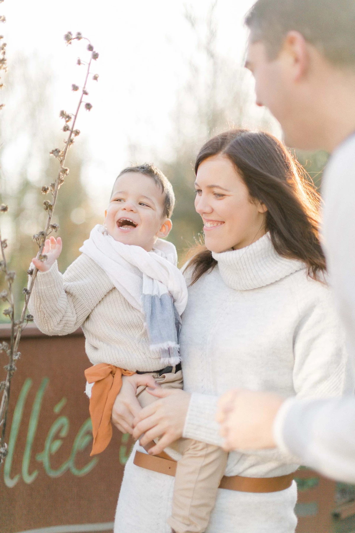 Séance photo famille en extérieur : parents et enfant en pulls beige et blanc devant branche fleurie, lumière douce et intemporelle
