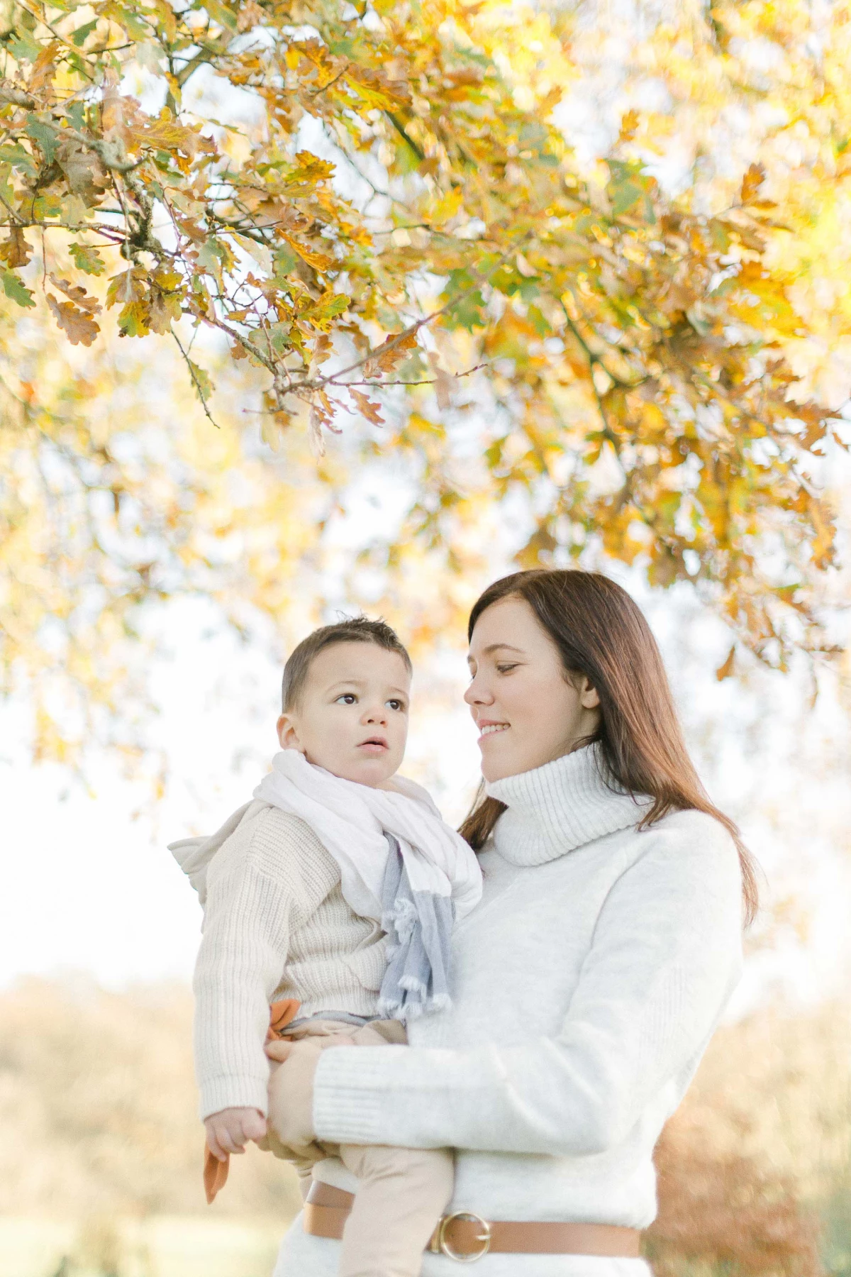 Séance famille automne : mère et enfant en pull blanc sous feuillage doré, complicité tendre et lumière chaleureuse