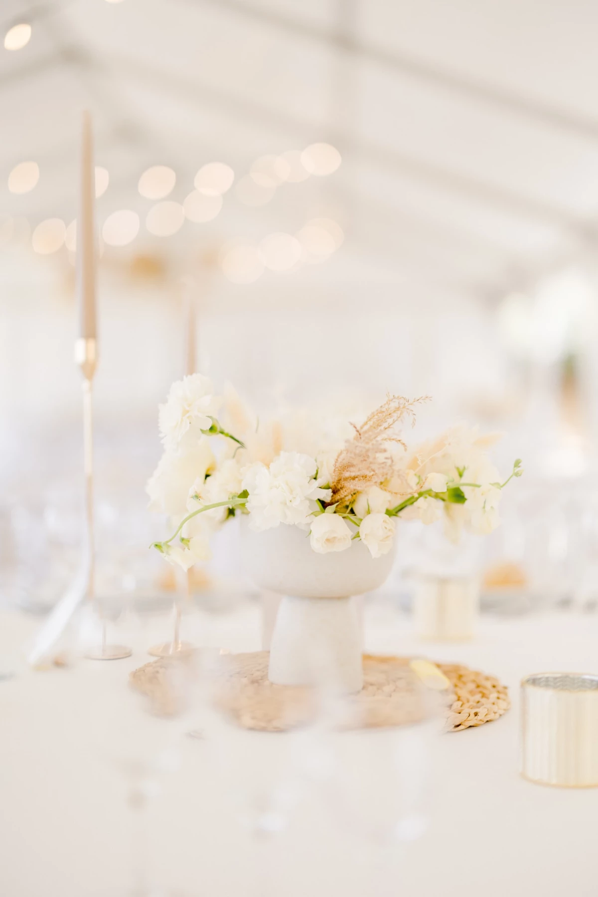 Composition florale délicate en blanc et beige sur table de mariage élégante avec bougies