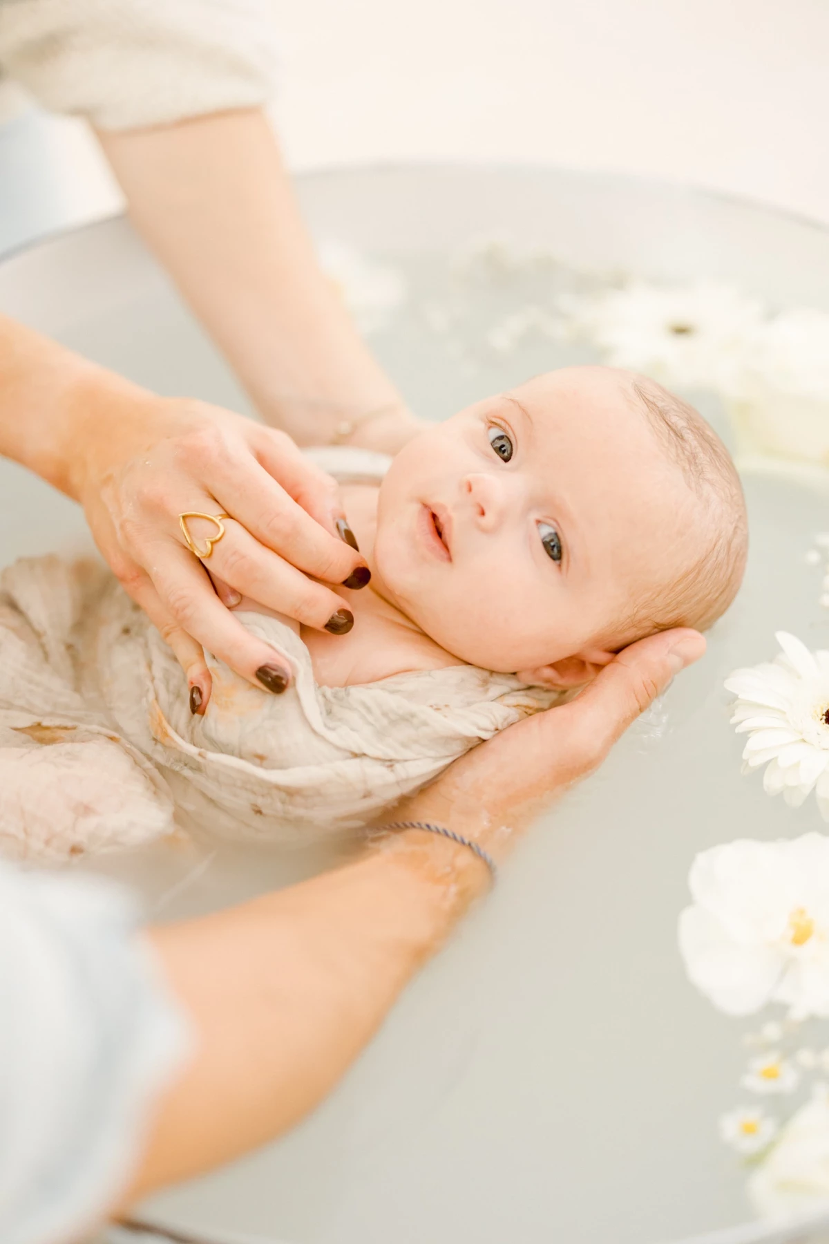 Séance nouveau-né au studio : bébé allongé dans un bain fleuri, mains maternelles délicates, ambiance de douceur infinie