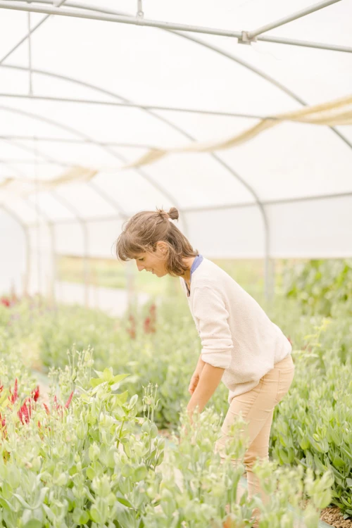 Petite fille en chemise blanche observant des fleurs dans une serre lumineuse au milieu de la verdure