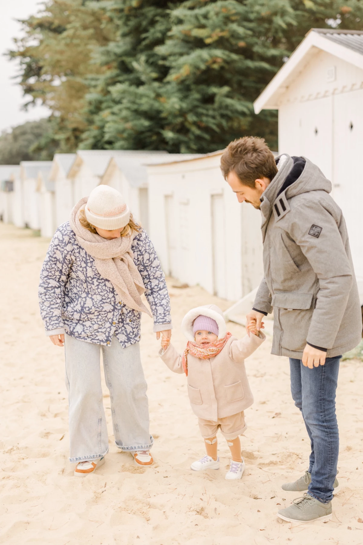 Père avec ses deux enfants se tenant la main sur une plage, ambiance hivernale douce et lumineuse