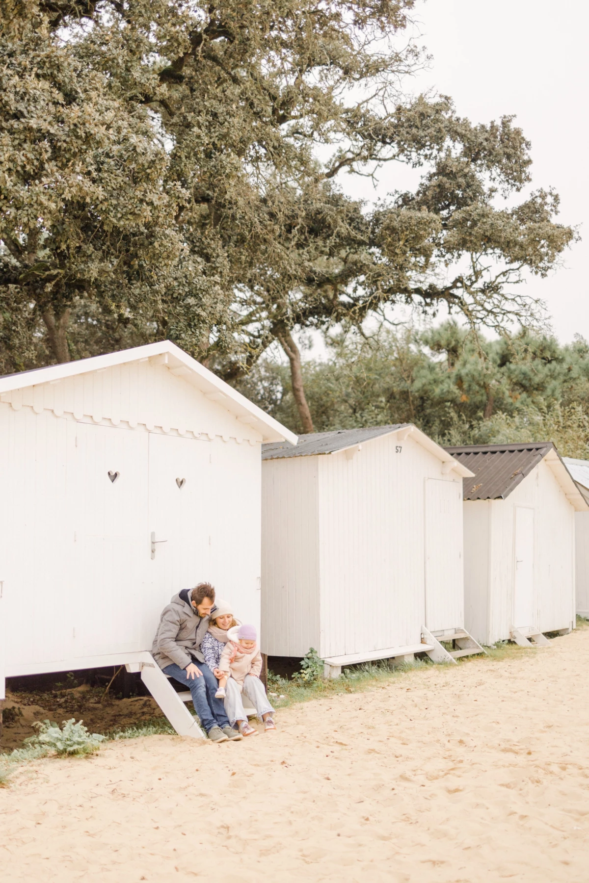 Mère et enfant partageant un moment tendre assis devant des cabanes de plage blanches