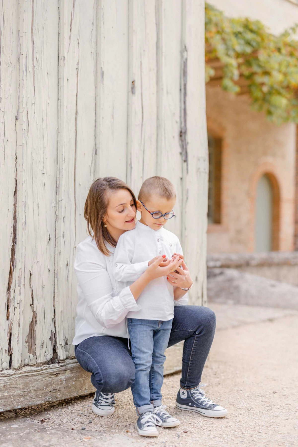 Séance photo famille : mère et petit garçon en complicité contre un mur blanc vintage, ambiance tendre et intemporelle dans une ruelle provençale