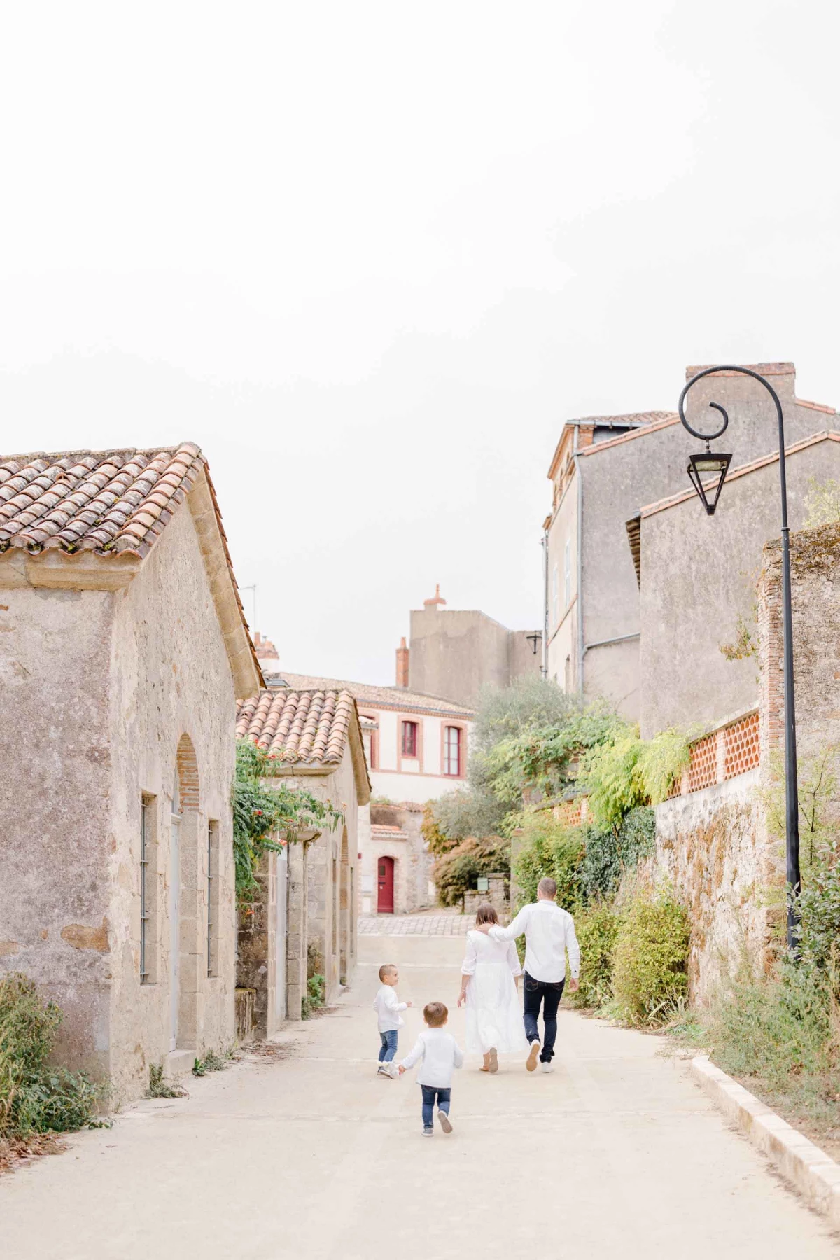Séance famille en Vendée : parents et enfants marchant dans une ruelle provençale pavée, lumière dorée, ambiance intemporelle et authentique