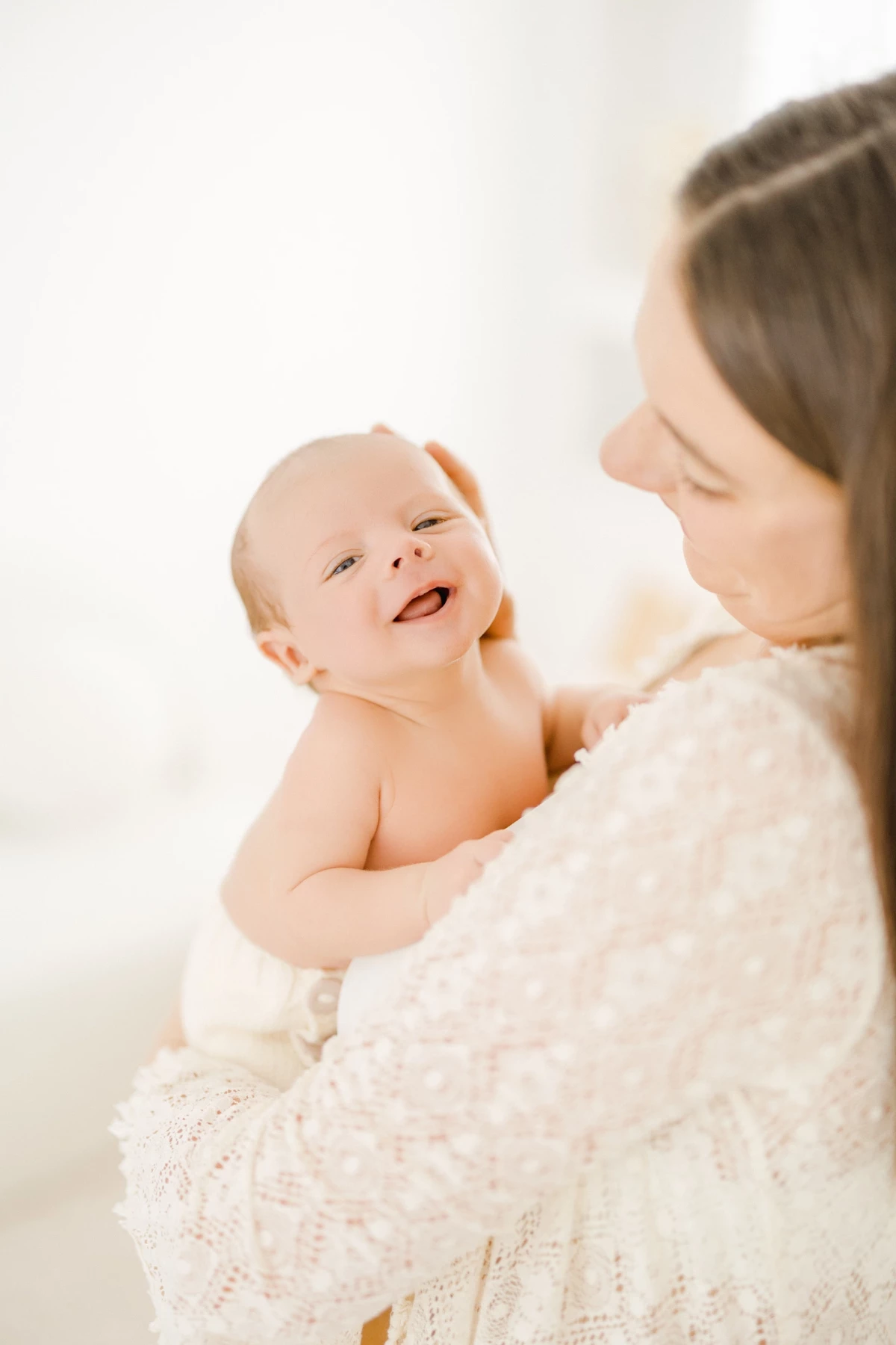 Séance naissance au studio : bébé souriant porté avec tendresse par sa maman, instant de bonheur et complicité maternelle