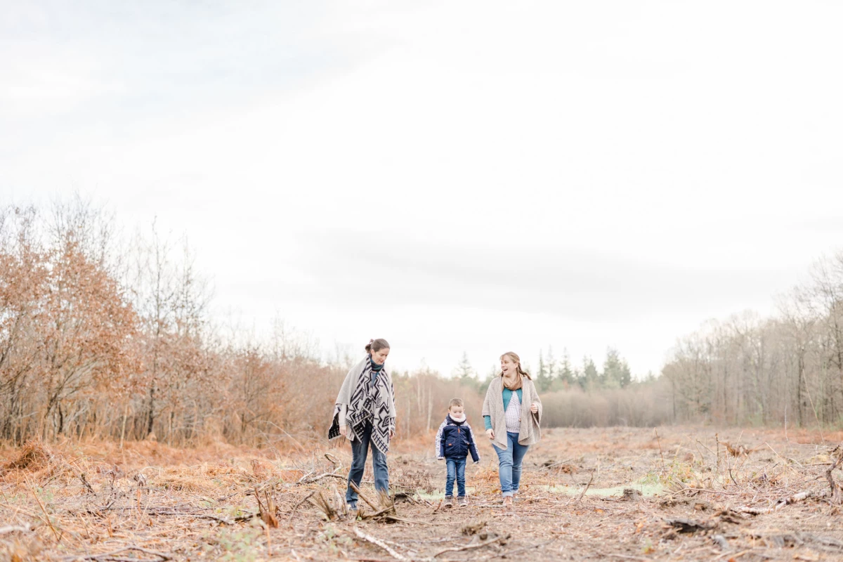Séance photo famille en extérieur automnal : parents et enfants marchent main dans la main dans un paysage boisé aux teintes chaudes, créant une atmosphère intemporelle d'authenticité et de complicité